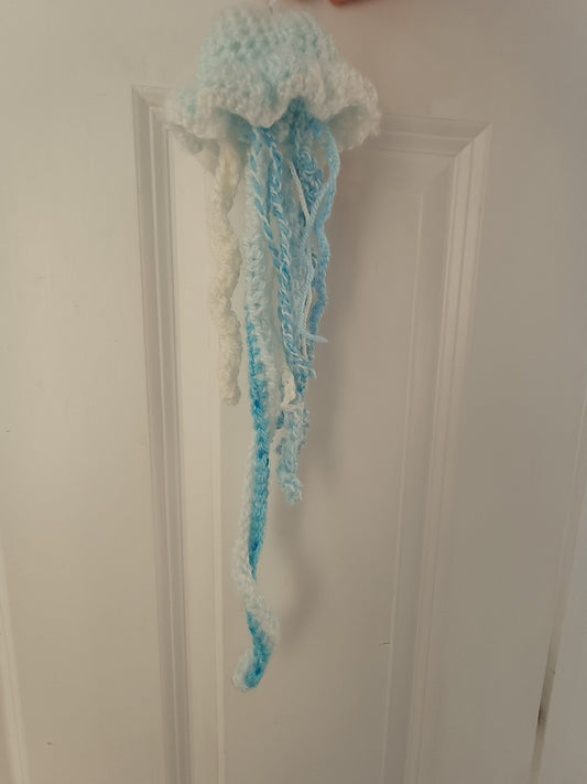 A handmade crochet jellyfish decoration in light blue and white yarn, hanging from a white paneled door.